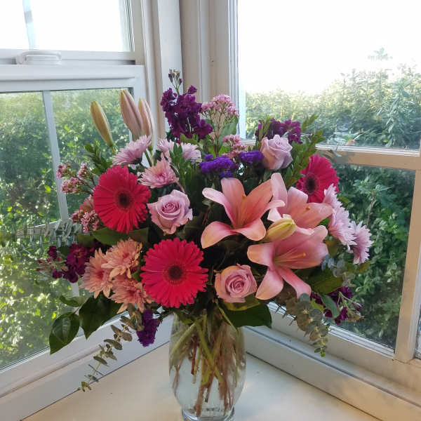 Mixed bouquet of pink lilies, roses, and gerbera daisies in a glass vase