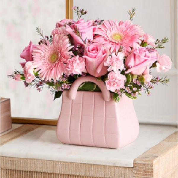 Pink roses, gerbera daisies, and carnations in a pink purse-shaped ceramic vase
