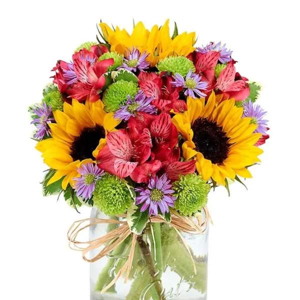 Mixed bouquet of sunflowers, red flowers, and purple daisies in a glass vase