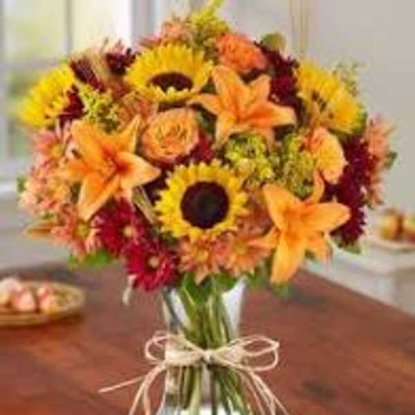 Bouquet of sunflowers, orange lilies, and mixed fall flowers in a glass vase