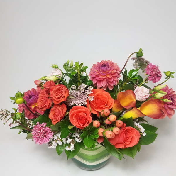 Mixed bouquet of orange and pink flowers in a striped glass vase