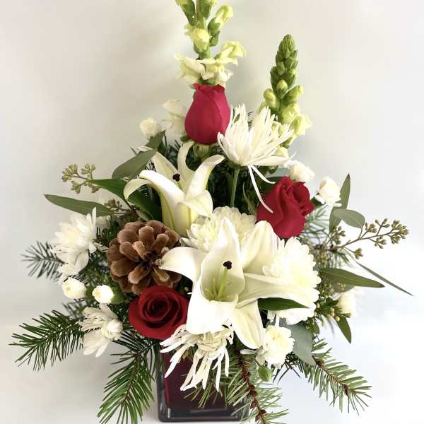 Red roses and white lilies in a square vase with pinecones