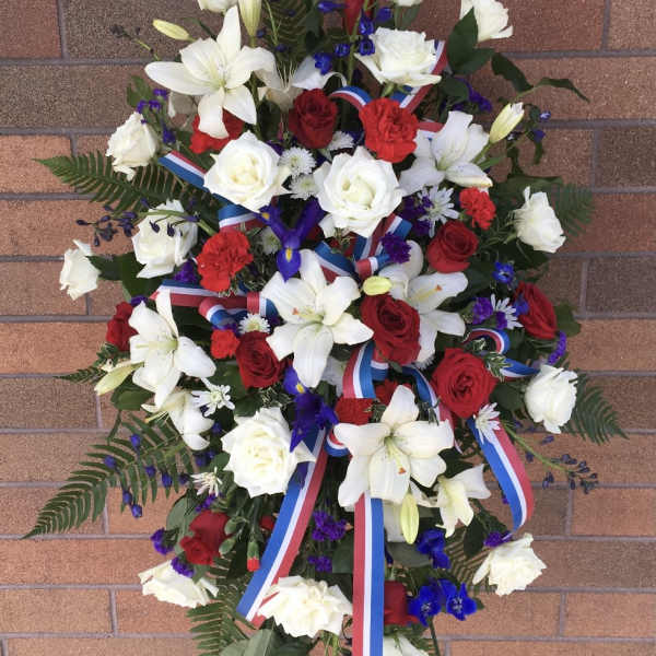 Standing floral spray with red and white roses, lilies, and ribbon streamers