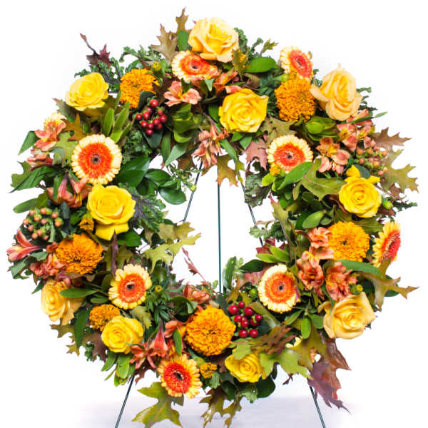 Autumn wreath of yellow roses, orange gerberas, and marigolds displayed on a metal stand