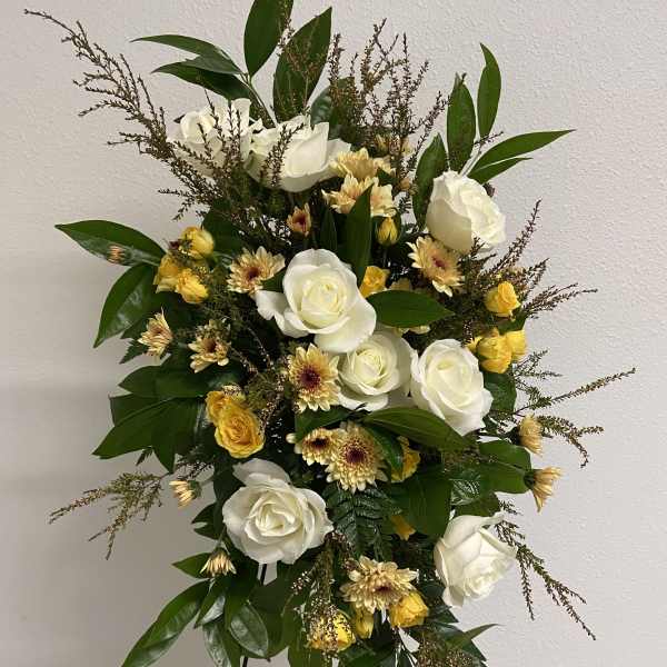 Standing spray of white roses and yellow flowers on a metal easel