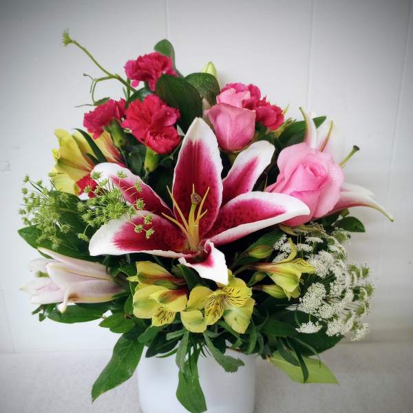 Mixed bouquet of pink roses, lilies, and carnations in a white vase