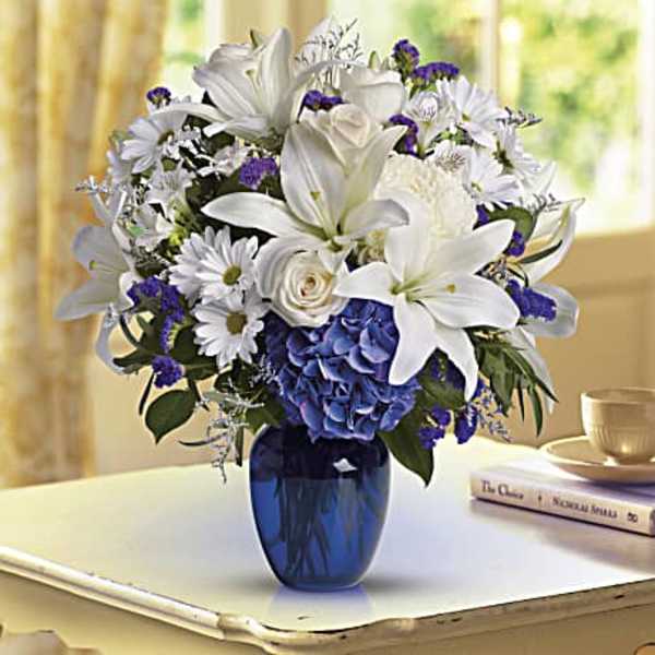 White lilies and daisies in a blue vase with blue hydrangea