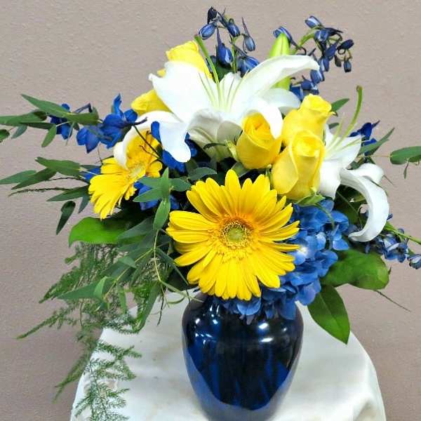 Bouquet of yellow roses, white lilies, and blue flowers in a dark vase
