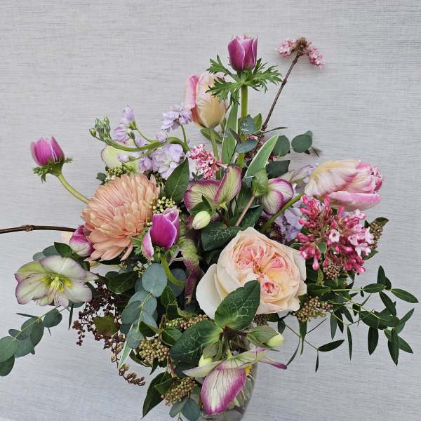 Loose arrangement of pink and peach blooms, including roses and tulips, in a clear glass vase