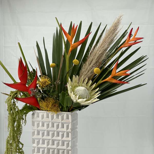 Tropical flower arrangement in a white geometric vase on a pedestal
