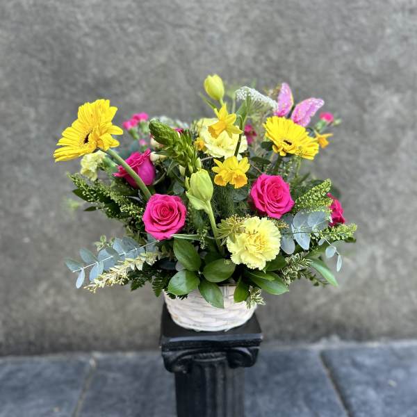 Bright mixed flower arrangement in a white basket with pink roses and yellow daisies