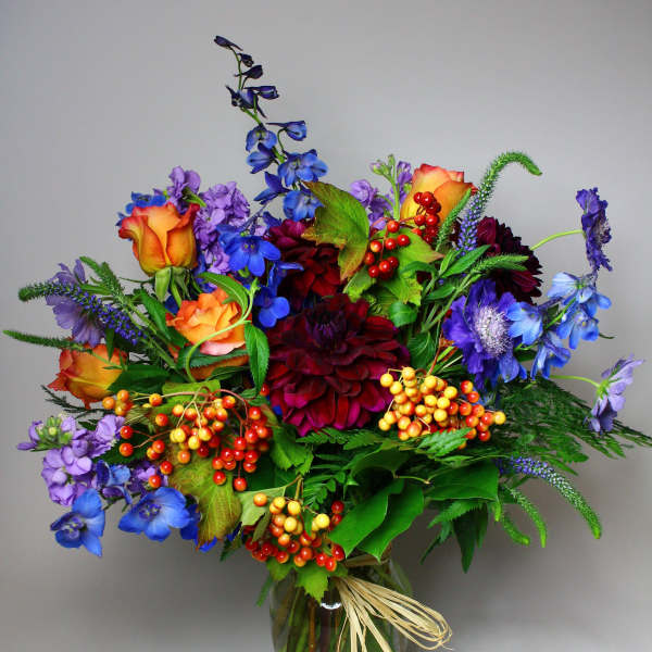 Colorful mixed bouquet in a glass vase with orange roses and blue flowers