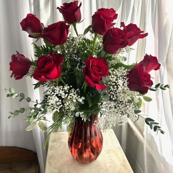 Red roses in a red glass vase with white filler flowers