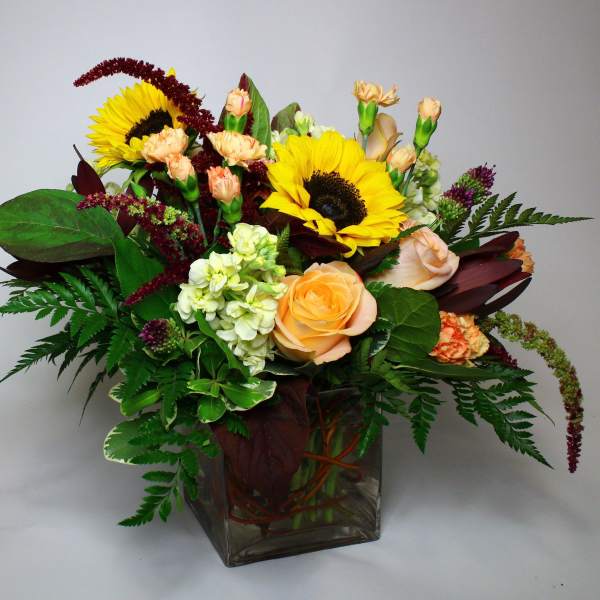 Bouquet of sunflowers, roses, and carnations in a square glass vase