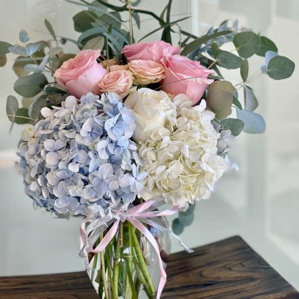 Pink roses and blue-white hydrangeas in a glass vase with ribbon