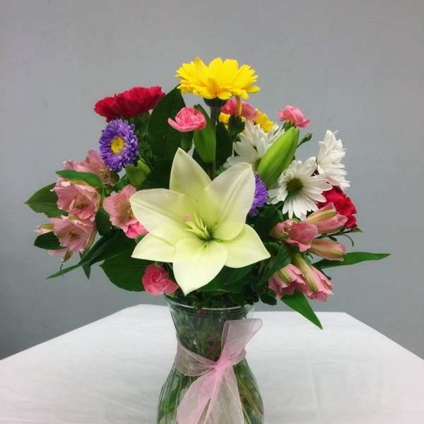 Mixed bouquet with a large white lily in a glass vase tied with pink ribbon