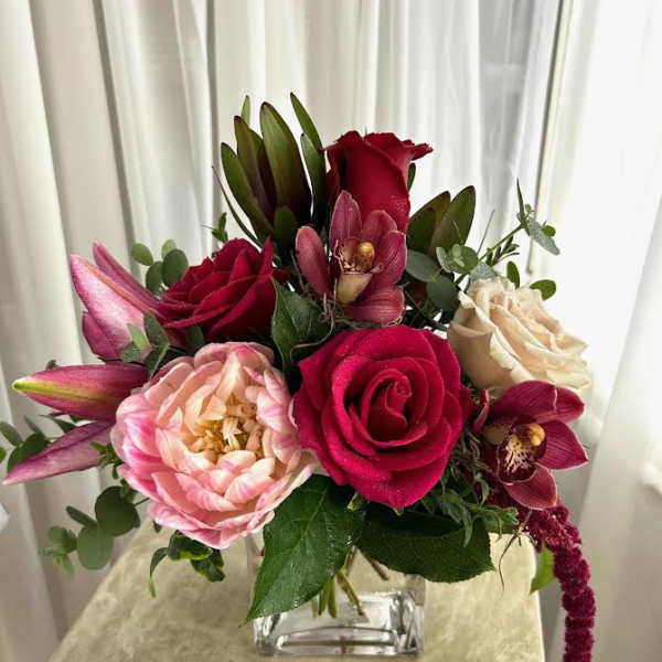 Bouquet of red and blush roses with orchids in a clear glass vase