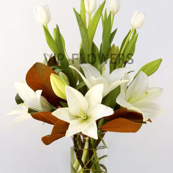 White lilies and tulips in a clear glass vase