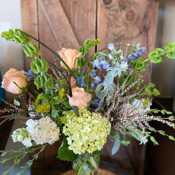 Tall vase arrangement with peach roses, green hydrangeas, bells of Ireland, and mixed accent flowers