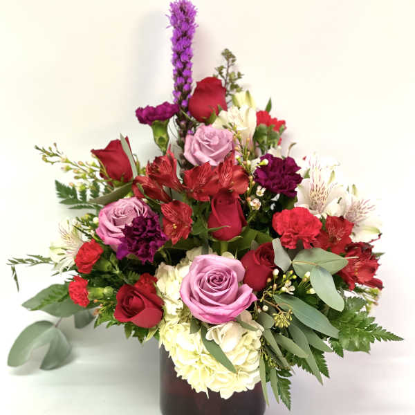 Mixed bouquet of roses, carnations, and alstroemeria in a dark vase