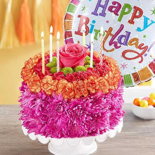 Flower-covered birthday cake with candles and a birthday balloon
