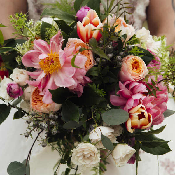 A bride holds a bouquet of pink, peach, and white flowers.