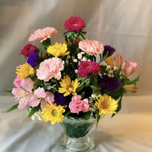 Mixed pink, yellow, and purple flowers arranged in a clear glass vase