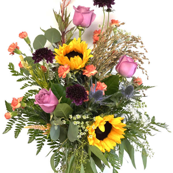 Mixed bouquet with sunflowers, pink roses, and dark purple blooms in a glass vase