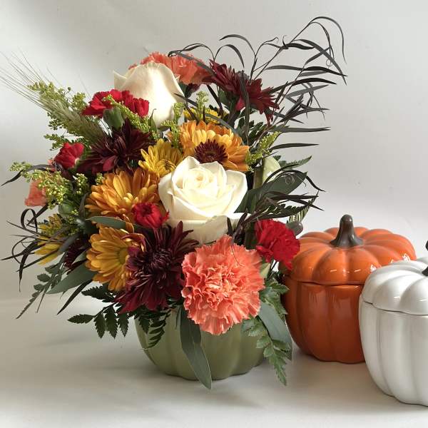 Mixed autumn bouquet in a green vase beside two pumpkin containers
