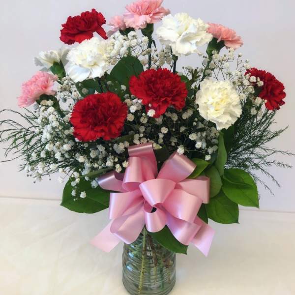 Bouquet of red, white, and pink carnations in a glass vase with a pink ribbon