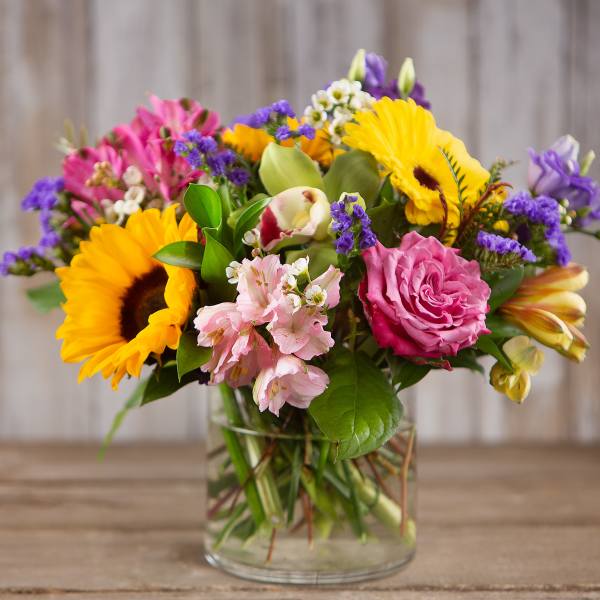 Mixed bouquet with sunflowers, pink roses, and purple blooms in a glass vase