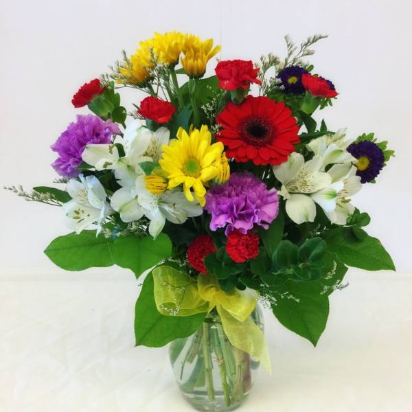Mixed bouquet of colorful flowers in a glass vase with a yellow ribbon