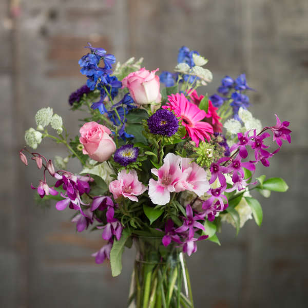 Mixed bouquet of pink, purple, and blue flowers in a clear glass vase