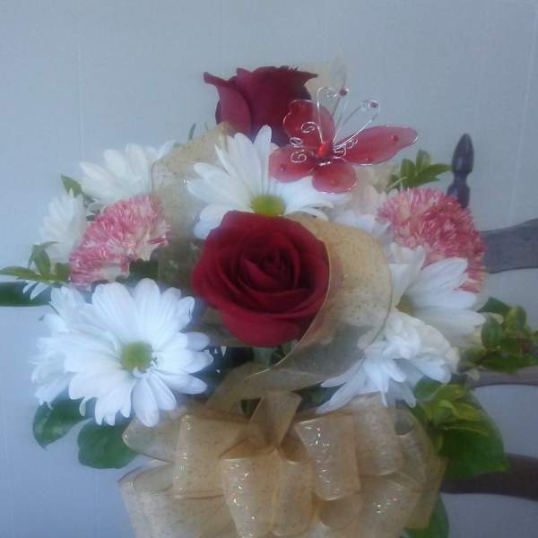 Mixed bouquet of red roses, white daisies, and pink carnations in a glass vase with gold bow and red butterfly pick