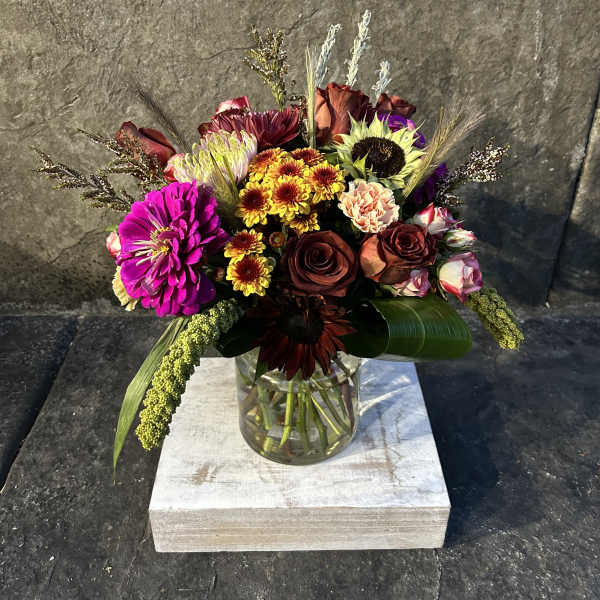 Mixed bouquet in a clear glass vase with bright blooms and dark roses
