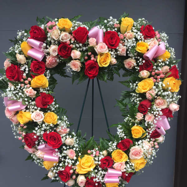 Heart-shaped wreath of red, yellow, and pink roses with ribbon accents