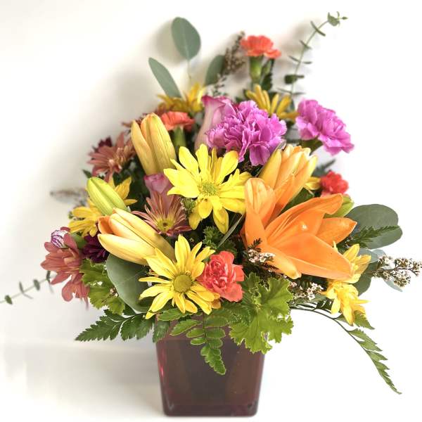 Mixed bouquet in a square vase with orange lilies and yellow daisies