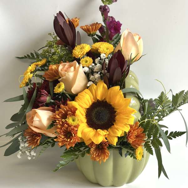 Mixed bouquet in a pale green pumpkin vase with a sunflower and peach roses