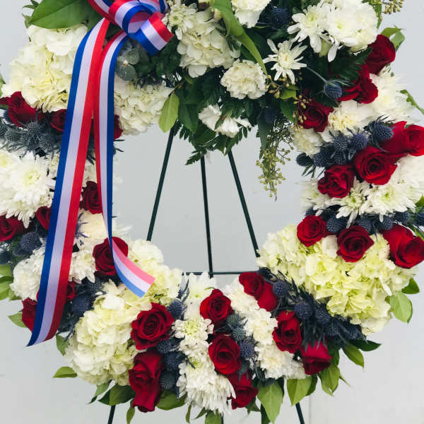 Floral wreath with red and white flowers and a tricolor ribbon on a stand