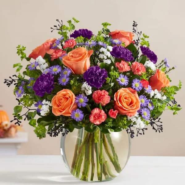 Bouquet of orange roses, purple flowers, and pink carnations in a glass vase