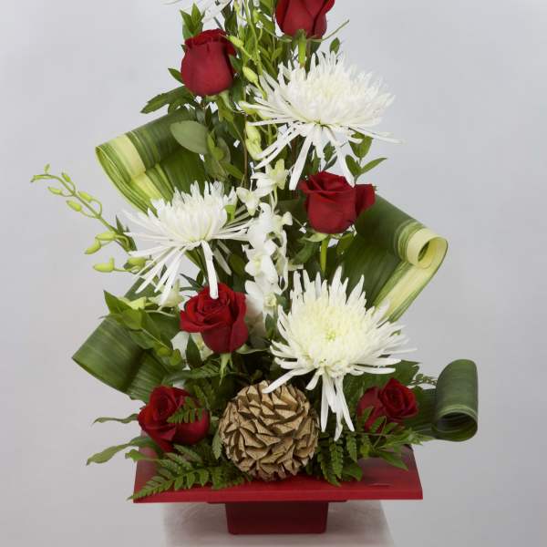 Red roses and white spider mums in a red vase with green leaf wrap