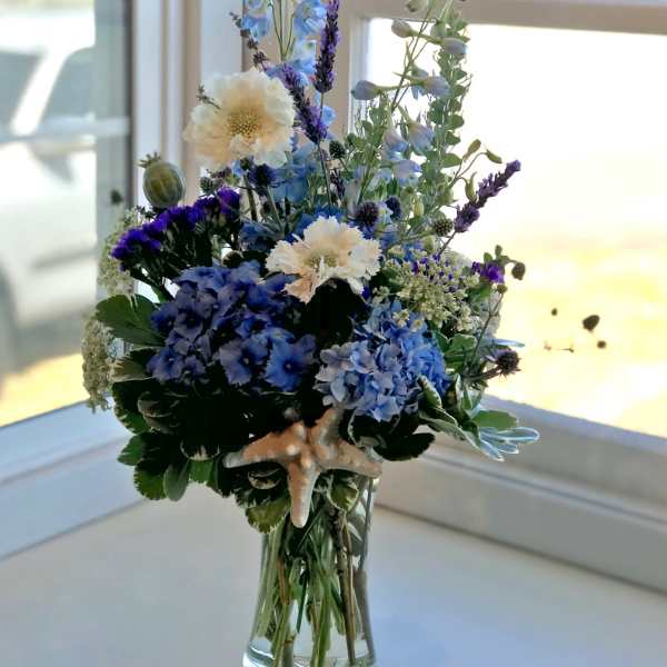 Blue and white floral arrangement in a clear glass vase with a starfish accent
