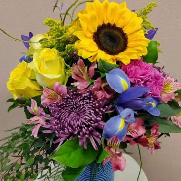 Colorful bouquet with sunflower, roses, and purple blooms in a blue vase