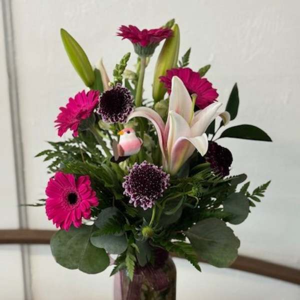 Pink gerbera and lily arrangement in a tall vase with a small bird ornament