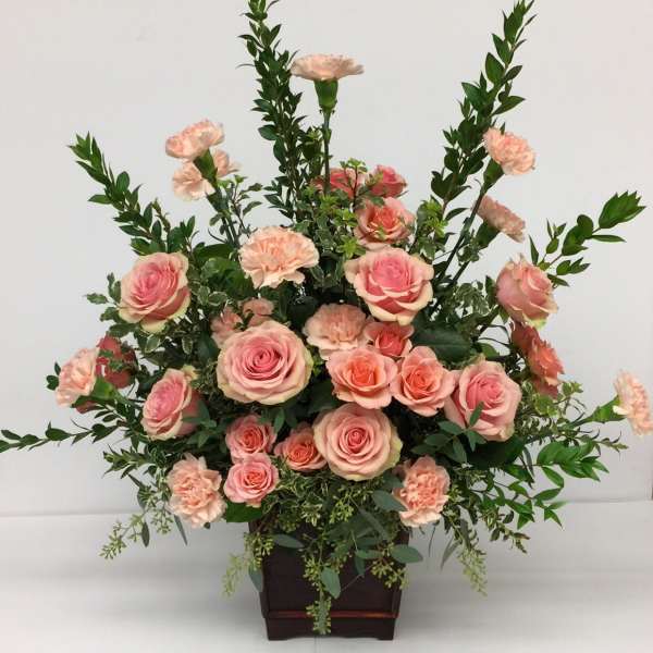 Pink roses and peach carnations arranged in a dark wooden container