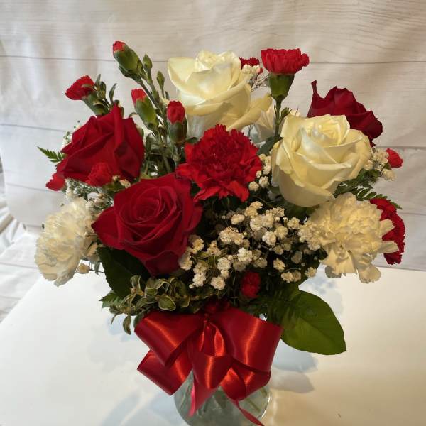 Red and white roses with carnations in a glass vase tied with a red ribbon