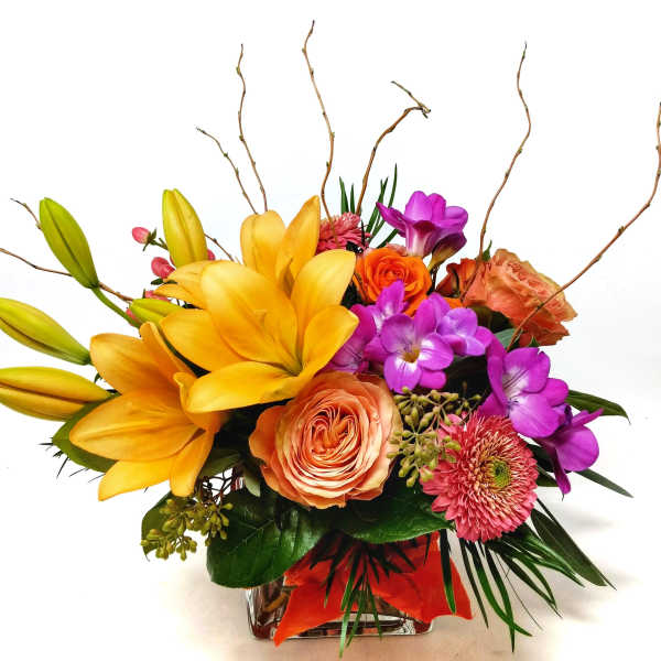Colorful bouquet with yellow lilies, orange roses, and purple flowers in a glass vase