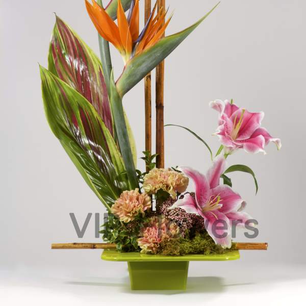 Tropical floral arrangement with orange bird-of-paradise and pink lilies in a green vase