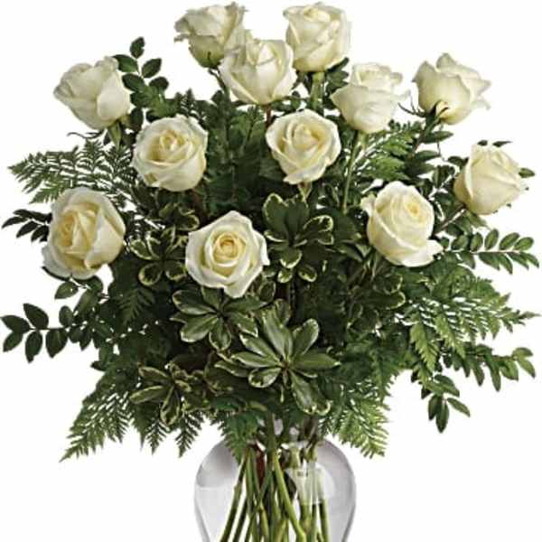 Arrangement of white roses with abundant green foliage in a clear glass vase