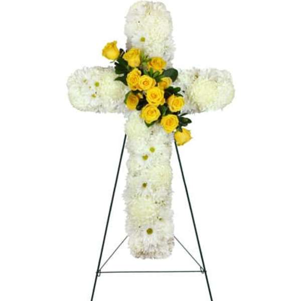 Standing floral cross of white mums with yellow roses at the center on a metal easel.